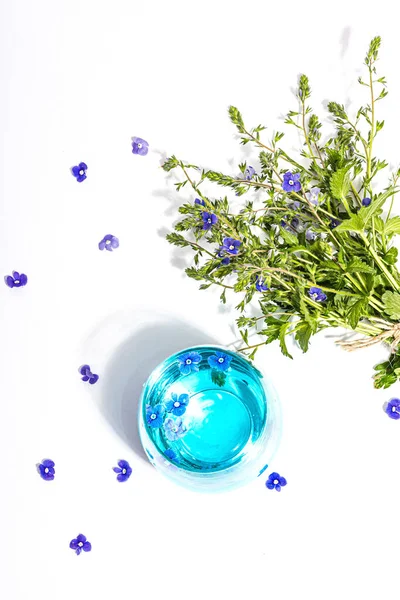 Cold tonic water and blue forget me not flowers bouquet isolated on a white background. Springtime concept, floral element, a hard light, dark shadow, selective focus, top view