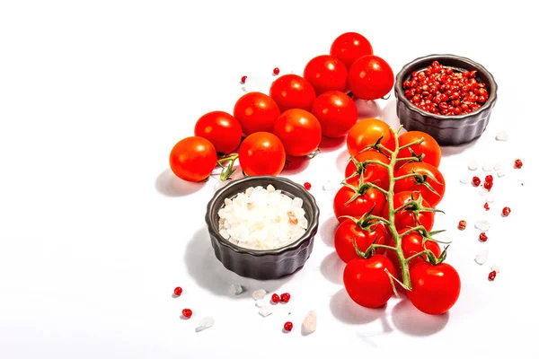 Cooking background with tomato cherry, sea salt, and rose peppercorn isolated on white background. A culinary concept with ripe vegetables and spices, copy space