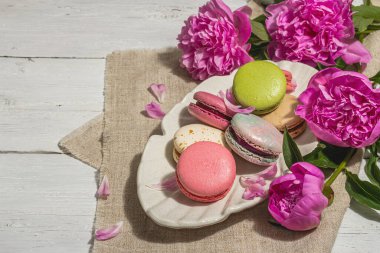 Beyaz ahşap arka planda şakayık demeti olan makarnalar. Tatlı tatlı, renkli ve pastel renkler, yaz konsepti. Romantik köy tarzı, şenlik kartı, sert ışık, karanlık gölge, kopyalama alanı