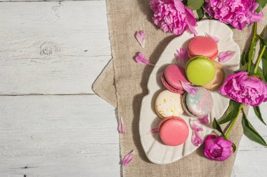 Beyaz ahşap arka planda şakayık demeti olan makarnalar. Tatlı tatlı, renkli ve pastel renkler, yaz konsepti. Romantik köy tarzı, şenlik kartı, sert ışık, koyu gölge, üst manzara