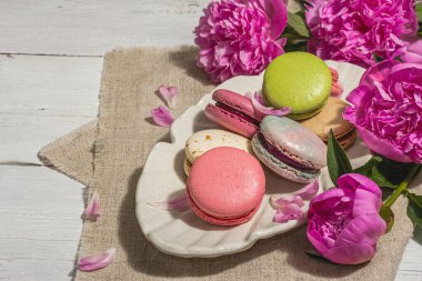 Beyaz ahşap arka planda şakayık demeti olan makarnalar. Tatlı tatlı, renkli ve pastel renkler, yaz konsepti. Romantik köy tarzı, şenlik kartı, sert ışık, karanlık gölge, kopyalama alanı