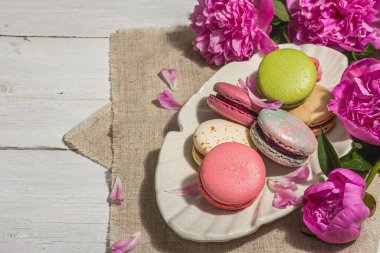 Beyaz ahşap arka planda şakayık demeti olan makarnalar. Tatlı tatlı, renkli ve pastel renkler, yaz konsepti. Romantik köy tarzı, şenlik kartı, sert ışık, karanlık gölge, kopyalama alanı