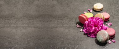 Taş bir arka planda şakayık çiçekli makarna. Tatlı, renkli ve pastel renkler. Romantik tarz, şenlik kartı, düz yatış, sert ışık, koyu gölge, afiş biçimi