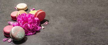 Taş bir arka planda şakayık çiçekli makarna. Tatlı, renkli ve pastel renkler. Romantik tarz, şenlik kartı, düz yatış, sert ışık, koyu gölge, afiş biçimi