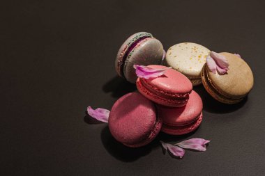 Siyah taşlı arka planda şakayık çiçekli makarna. Tatlı, renkli ve pastel renkler. Romantik tarz, şenlik kartı, düz yatış, sert ışık, karanlık gölge, kopyalama alanı