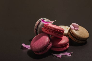 Siyah taşlı arka planda şakayık çiçekli makarna. Tatlı, renkli ve pastel renkler. Romantik tarz, şenlik kartı, düz yatış, sert ışık, karanlık gölge, kopyalama alanı