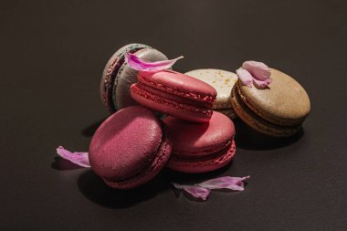 Siyah taşlı arka planda şakayık çiçekli makarna. Tatlı, renkli ve pastel renkler. Romantik tarz, şenlik kartı, düz yatış, sert ışık, karanlık gölge, kopyalama alanı