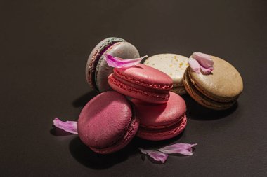 Siyah taşlı arka planda şakayık çiçekli makarna. Tatlı, renkli ve pastel renkler. Romantik tarz, şenlik kartı, düz yatış, sert ışık, karanlık gölge, kopyalama alanı