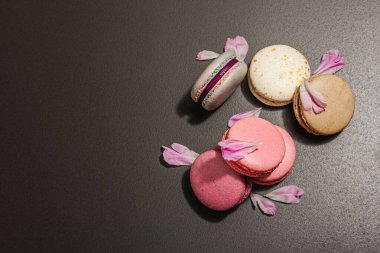 Siyah taşlı arka planda şakayık çiçekli makarna. Tatlı, renkli ve pastel renkler. Romantik tarz, şenlik kartı, düz yatış, sert ışık, koyu gölge, üst manzara