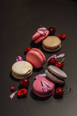 Şakayık çiçekli makarna ve siyah taştan bir arka planda olgun kirazlar. Tatlı tatlı, romantik stil, şenlik kartı, düz yatış, sert ışık, karanlık gölge, kapat