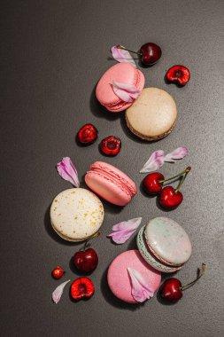 Şakayık çiçekli makarna ve siyah taştan bir arka planda olgun kirazlar. Tatlı tatlı, romantik stil, şenlik kartı, düz yatış, sert ışık, koyu gölge, üst manzara