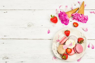 Beyaz ahşap arka planda çilek ve şakayık çiçekli makarna. Tatlı tatlı, romantik tarzı, düz yatış, sert ışık, koyu gölge, üst manzara