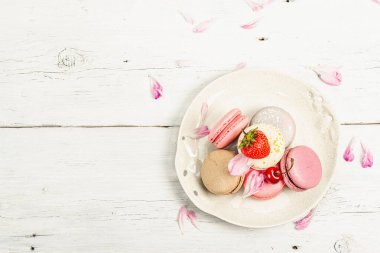 Beyaz ahşap bir arka planda çilekli, kirazlı ve şakayıklı çiçek yaprakları. Tatlı tatlı, romantik tarzı, düz yatış, sert ışık, koyu gölge, üst manzara