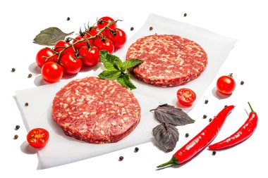 Beyaz arka planda izole edilmiş kıymalı biftekten çiğ pirzola. Taze sebze, fesleğen ve baharat. Modaya uygun sert bir ışık, karanlık bir gölge.