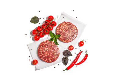 Beyaz arka planda izole edilmiş kıymalı biftekten çiğ pirzola. Taze sebze, fesleğen ve baharat. Modaya uygun bir aydınlık, karanlık gölge, üst manzara.