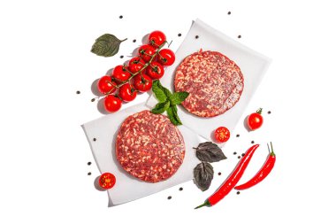 Beyaz arka planda izole edilmiş kıymalı biftekten çiğ pirzola. Taze sebze, fesleğen ve baharat. Modaya uygun bir aydınlık, karanlık gölge, üst manzara.