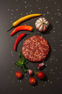 Siyah taşlı arka planda kıymalı biftek pirzolası. Taze sebze, nane ve baharat. Modern sert ışık, karanlık gölge, düz uzanma, üst manzara
