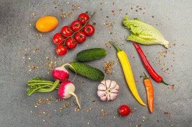Yemek malzemeleri arka planında. Baharatlar, sebzeler, sarımsak, renkli biber ve salatalık. Taş beton arka plan, hazır yiyecek konsepti, düz alan, üst manzara