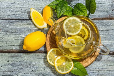 Lemon tea with ripe fruits and fresh leaves. Healthy morning breakfast, rustic style, wooden background. Hot beverage in a glass teapot, hard light, dark shadow, flat lay, top view