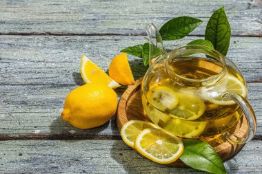 Olgun meyveli ve taze yapraklı limon çayı. Sağlıklı sabah kahvaltısı, köy tarzı, ahşap arka plan. Sıcak içecek cam çaydanlıkta, sert ışık, karanlık gölge, düz yer, kopyalama alanı