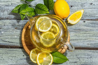 Olgun meyveli ve taze yapraklı limon çayı. Sağlıklı sabah kahvaltısı, köy tarzı, ahşap arka plan. Sıcak içecek cam çaydanlıkta, sert ışık, koyu gölge, düz uzanma, üst manzara