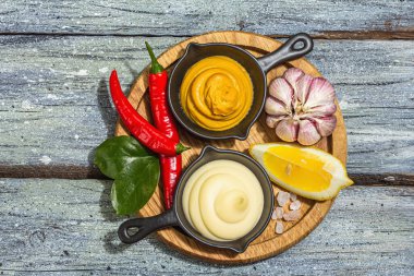 Mustard and mayonnaise sauces. Fresh mint, lemon, garlic, and spices. A hard light, dark shadow, wooden boards background, flat lay, top view
