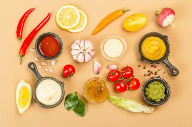 Bej arka planda soslar ve taze sebzeler. Ketçap, hardal, mayonez, wasabi, tatlı köri ve barbekü. Baharatlar ve otlar, üst manzara.