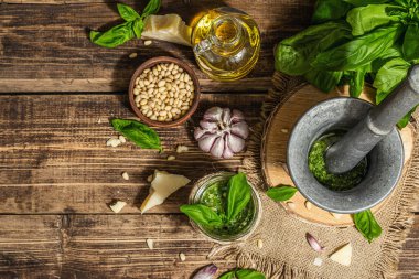 Ev yapımı İtalyan fesleğenli pesto sosu. Kaliteli havan topuzlu. Taze yaprak, parmesan, çam fıstığı ve zeytinyağı. Modaya uygun sert ışık, karanlık gölge, eski ahşap arka plan, üst manzara