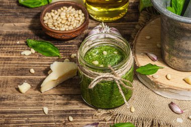 Ev yapımı İtalyan fesleğenli pesto sosu. Kaliteli havan topuzlu. Taze yaprak, parmesan, çam fıstığı ve zeytinyağı. Modaya uygun sert ışık, karanlık gölge, eski ahşap arka plan, kapat