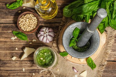 Ev yapımı İtalyan fesleğenli pesto sosu. Kaliteli havan topuzlu. Taze yaprak, parmesan, çam fıstığı ve zeytinyağı. Modaya uygun sert ışık, karanlık gölge, eski ahşap arka plan, üst manzara