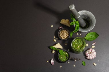 Antika havan topuzlu İtalyan fesleğen sosu hazırlama işlemi. Ev yapımı yemekler, geleneksel tarifler için malzemeler. Sert ışık, karanlık gölge, siyah taş arka plan, üst görüş