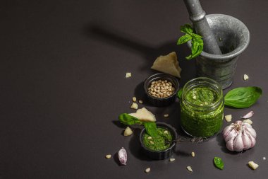 Antika havan topuzlu İtalyan fesleğen sosu hazırlama işlemi. Ev yapımı yemekler, geleneksel tarifler için malzemeler. Sert ışık, koyu gölge, siyah taş arkaplan, boşluğu kopyala