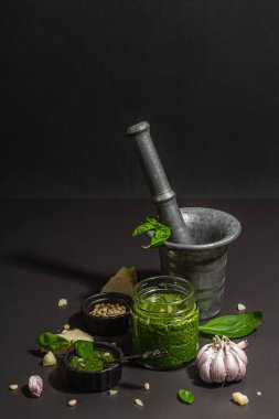 Antika havan topuzlu İtalyan fesleğen sosu hazırlama işlemi. Ev yapımı yemekler, geleneksel tarifler için malzemeler. Sert ışık, koyu gölge, siyah taş arkaplan, boşluğu kopyala