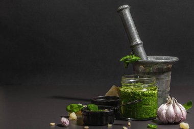 Antika havan topuzlu İtalyan fesleğen sosu hazırlama işlemi. Ev yapımı yemekler, geleneksel tarifler için malzemeler. Sert ışık, koyu gölge, siyah taş arkaplan, boşluğu kopyala