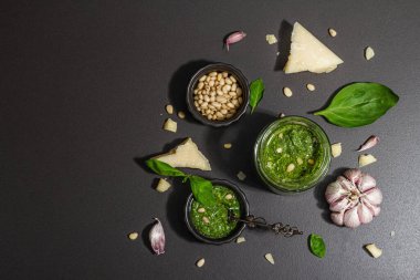 Klasik İtalyan fesleğen sosu cam kavanozda. Ev yapımı yemekler, geleneksel tarifler için malzemeler. Sert ışık, karanlık gölge, siyah taş arka plan, üst görüş