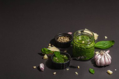 Klasik İtalyan fesleğen sosu cam kavanozda. Ev yapımı yemekler, geleneksel tarifler için malzemeler. Sert ışık, koyu gölge, siyah taş arkaplan, boşluğu kopyala