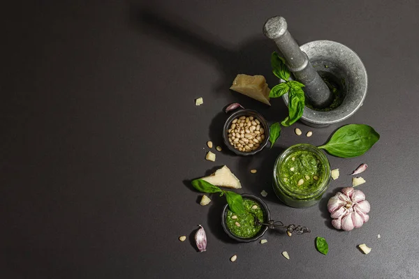 Antika havan topuzlu İtalyan fesleğen sosu hazırlama işlemi. Ev yapımı yemekler, geleneksel tarifler için malzemeler. Sert ışık, karanlık gölge, siyah taş arka plan, üst görüş