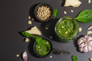 Klasik İtalyan fesleğen sosu cam kavanozda. Ev yapımı yemekler, geleneksel tarifler için malzemeler. Sert ışık, karanlık gölge, siyah taş arka plan, üst görüş