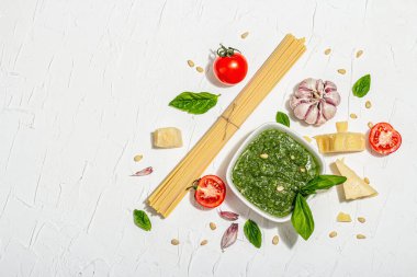 Klasik İtalyan makarnası hazırlamak için geleneksel malzemeler. Kuru spagetti, fesleğen sosu, domates kirazı, parmesan ve sarımsak. Moda sert ışık, koyu gölge, beyaz macun arkaplan, üst görünüm