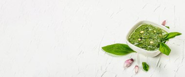 Çam fıstığı, parmesan ve sarımsaklı bir kasede pesto sosu. Modaya uygun sert ışık, koyu gölge, beyaz macun arkaplan, pankart biçimi