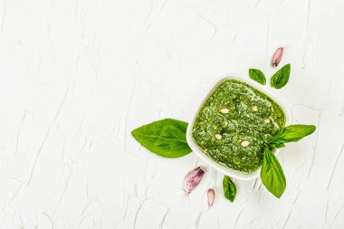 Çam fıstığı, parmesan ve sarımsaklı bir kasede pesto sosu. Moda sert ışık, koyu gölge, beyaz macun arkaplan, üst görünüm