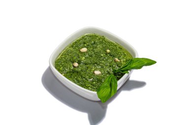 Beyaz arka planda çam fıstığı, parmesan ve sarımsak ile kaplı bir kasede pesto sosu. Modaya uygun sert ışık, karanlık gölge, düz uzanma