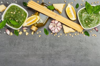 Klasik İtalyan makarnası hazırlamak için geleneksel malzemeler. Kuru spagetti, fesleğen pesto, parmesan, limon ve sarımsak. Gri taş arkaplan, üst manzara
