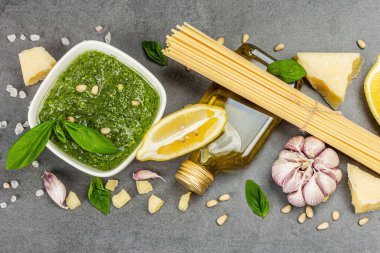 Klasik İtalyan makarnası hazırlamak için geleneksel malzemeler. Kuru spagetti, fesleğen pesto, parmesan, limon ve sarımsak. Gri taş arkaplan, üst manzara