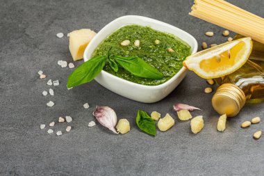 Traditional ingredients for the preparation of classic Italian pasta. Dry spaghetti, basil pesto, parmesan, lemon and garlic. Grey stone concrete background, copy space