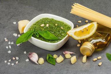 Klasik İtalyan makarnası hazırlamak için geleneksel malzemeler. Kuru spagetti, fesleğen pesto, parmesan, limon ve sarımsak. Gri taş beton arka plan, kapat