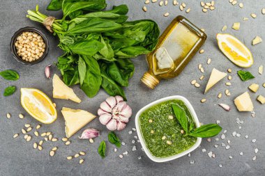 Pesto sauce in a bowls with pine nuts, parmesan and garlic. Traditional Italian food, grey stone concrete background, banner format, top view