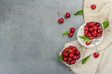Taze nane yapraklı olgun kirazlar, geleneksel yaz meyveleri. Modaya uygun beton standları, kaliteli peçeteler. Gri taş arkaplan, üst manzara