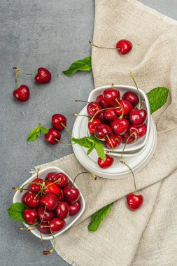 Taze nane yapraklı olgun kirazlar, geleneksel yaz meyveleri. Modaya uygun beton standları, kaliteli peçeteler. Gri taş arkaplan, üst manzara