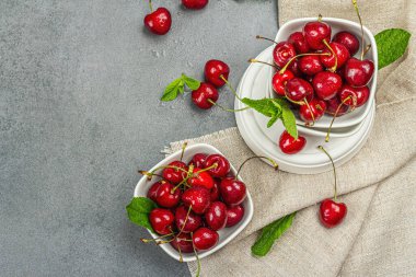 Taze nane yapraklı olgun kirazlar, geleneksel yaz meyveleri. Modaya uygun beton standları, kaliteli peçeteler. Gri taş arkaplan, üst manzara